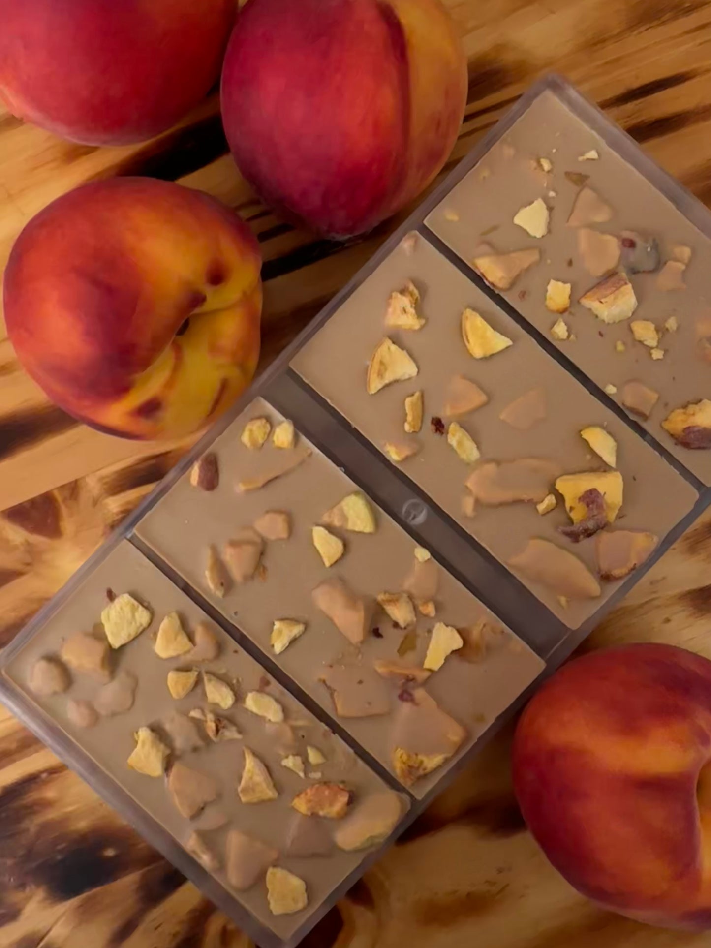 4 chocolate bars studded with pieces of peaches and surrounded by gorgeous ripe peaches.